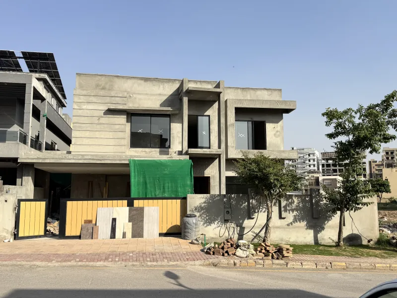 House under construction at grey structure — RCC frame complete, materials stacked on site